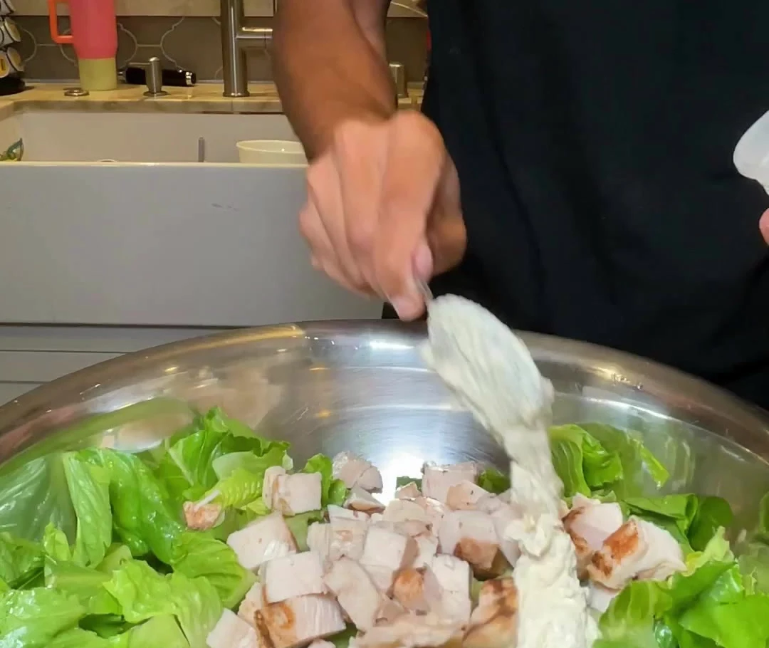 Homemade Caesar dressing being added to romaine and cooked chicken